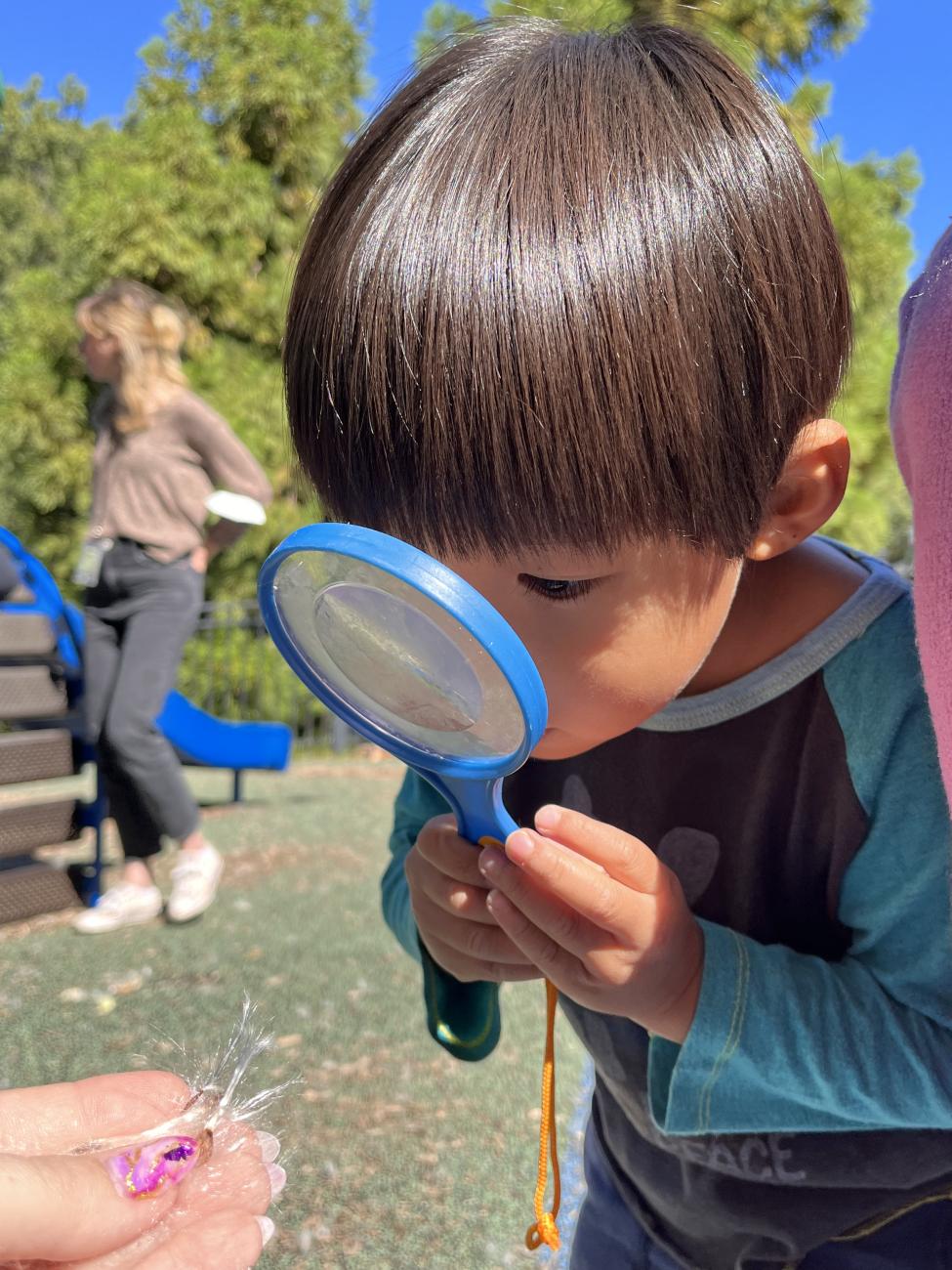 A child holds a magnifying glass near his face to see something up close.